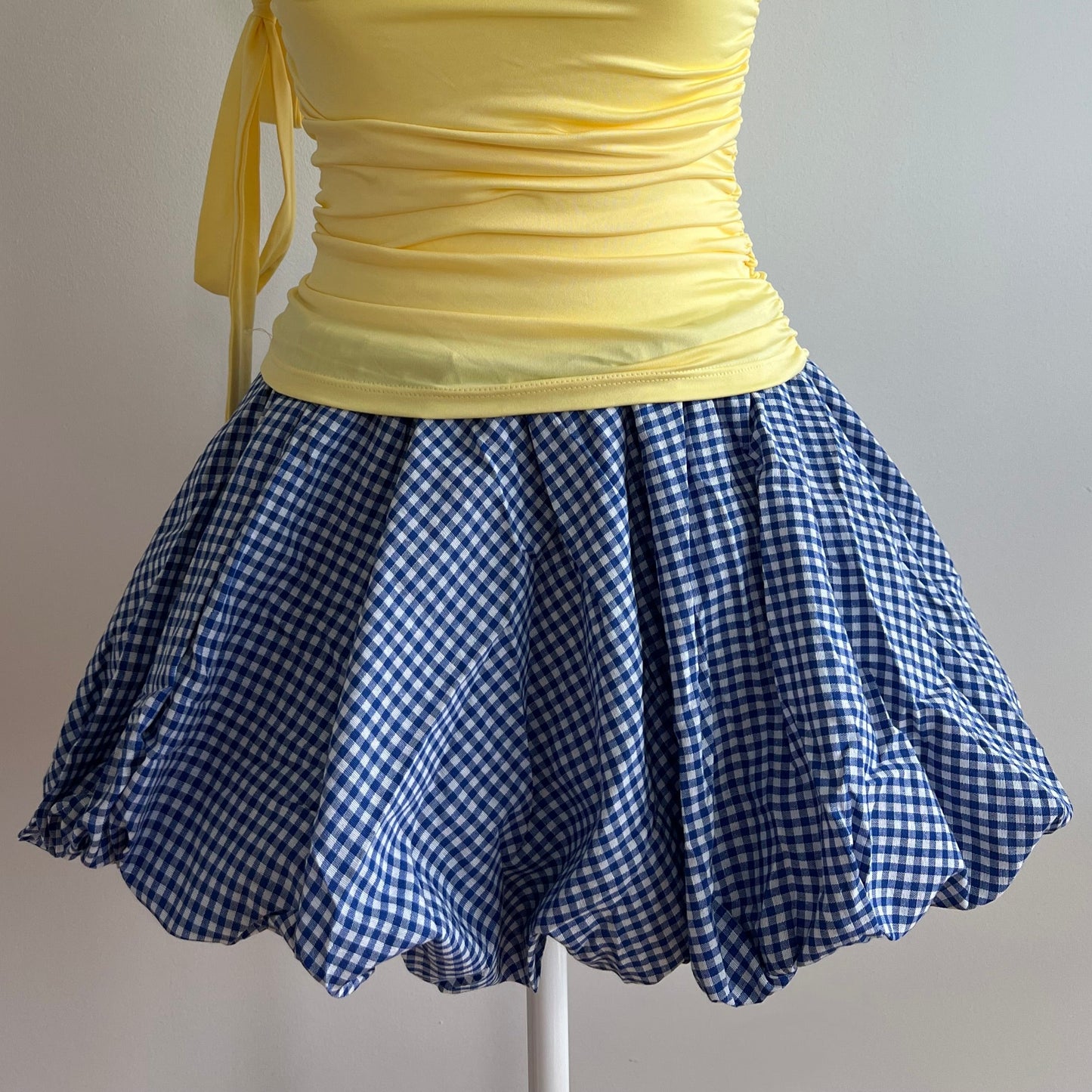 Bubble Blue Checker Skirt, a balloon mini skirt in a gingham blue pattern. Designed with an elastic waist for comfort and a structured hem that holds its shape, it’s perfect for pairing with fitted tops, baby tees, or tights for a coquette or Y2K-inspired look.
Model is wearing size S (US 0–2).