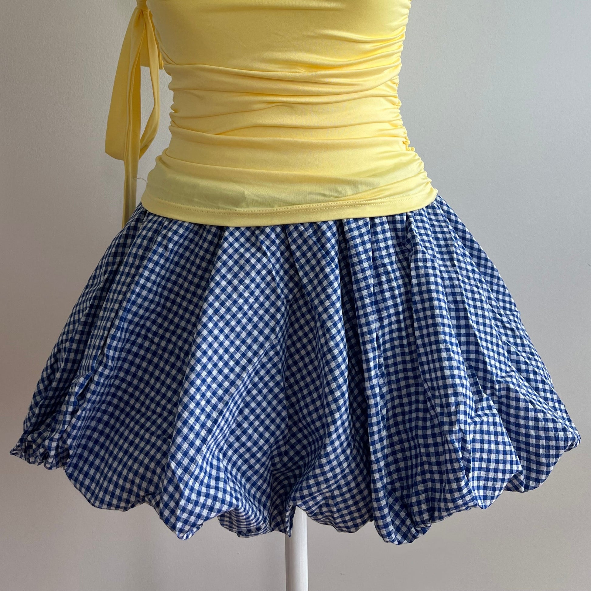 Bubble Blue Checker Skirt, a balloon mini skirt in a gingham blue pattern. Designed with an elastic waist for comfort and a structured hem that holds its shape, it’s perfect for pairing with fitted tops, baby tees, or tights for a coquette or Y2K-inspired look.
Model is wearing size S (US 0–2).