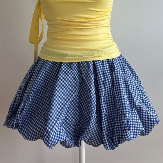 Bubble Blue Checker Skirt, a balloon mini skirt in a gingham blue pattern. Designed with an elastic waist for comfort and a structured hem that holds its shape, it’s perfect for pairing with fitted tops, baby tees, or tights for a coquette or Y2K-inspired look.
Model is wearing size S (US 0–2).