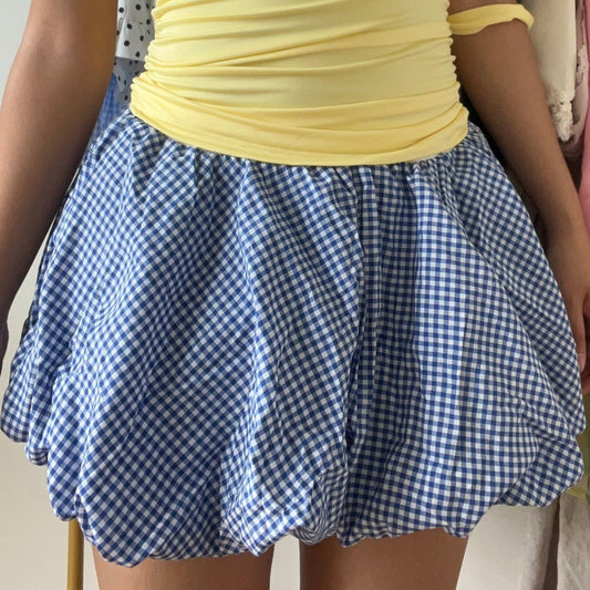 Bubble Blue Checker Skirt, a balloon mini skirt in a gingham blue pattern. Designed with an elastic waist for comfort and a structured hem that holds its shape, it’s perfect for pairing with fitted tops, baby tees, or tights for a coquette or Y2K-inspired look.

Model is wearing size S (US 0–2).
